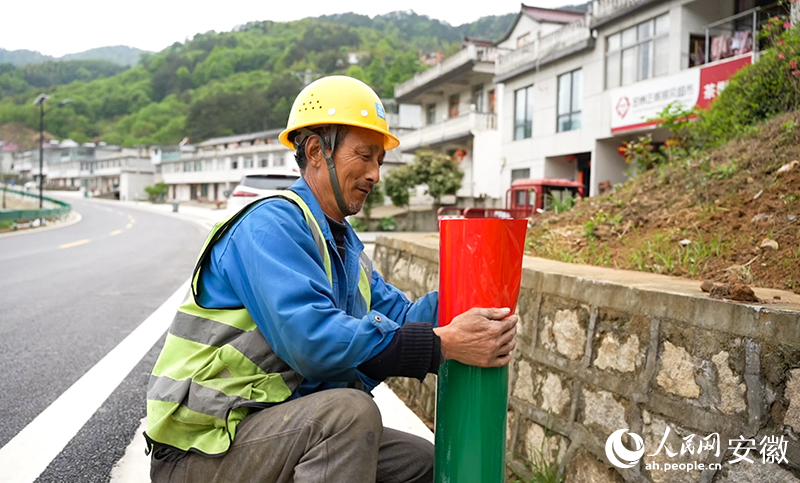 大灣村村民陶元佳正在路邊為護(hù)欄張貼反光貼。人民網(wǎng)記者 王銳攝