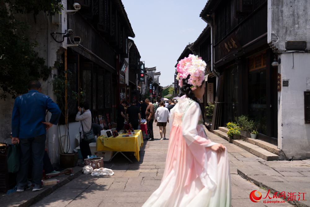 5月26日，浙江省嘉興市月河街上游人如織，一名身著傳統(tǒng)服飾的年輕女子從鏡頭前走過。人民網(wǎng)記者 葛泰佚攝